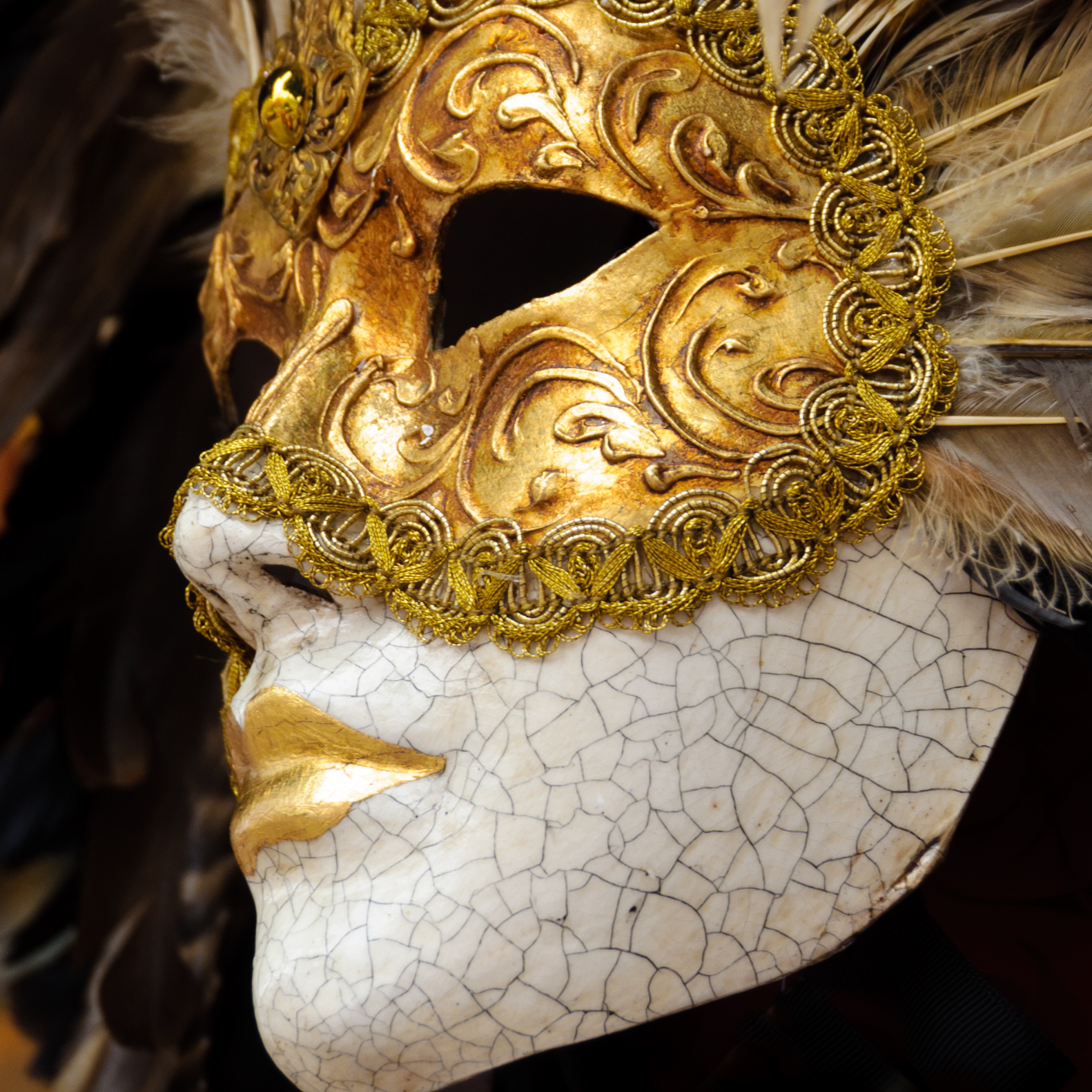 Máscara de mujer con tonos dorados y blancos y plumas alrededor de la máscara. Esta y más máscaras en nuestra tienda online de arte