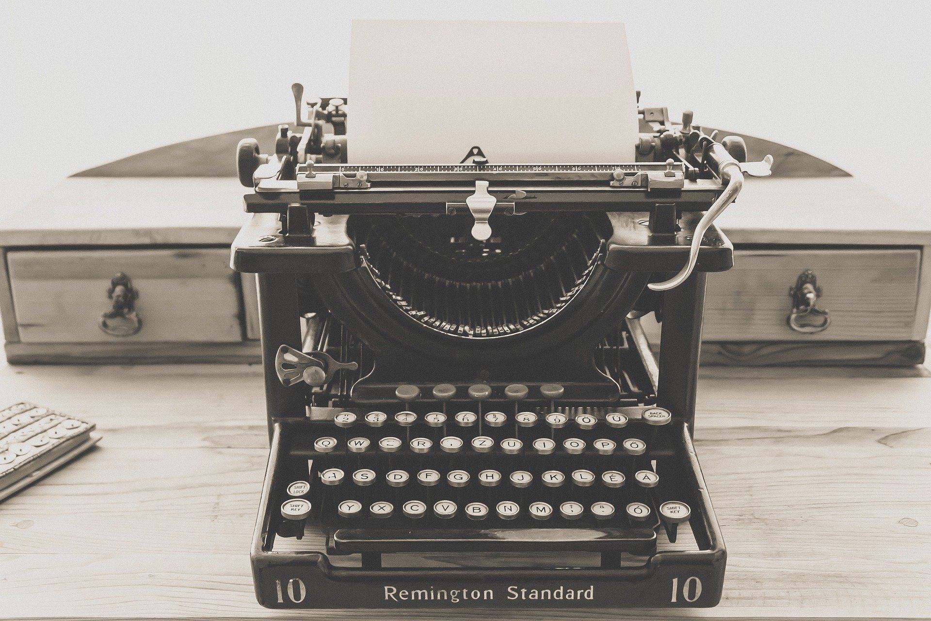 Una Remington Standard, una de las clásicas máquinas de escribir cuyas letras podrás encontrar en nuestra tienda online de arte, con un folio en blanco y sobre un escritorio de madera